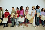 Middle school kids holding their trays wait in a school lunch line.