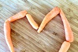 Fresh carrots laid out on a wooden tabletop in the shape of a heart.