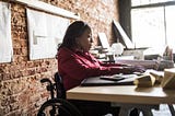 A Black businesswoman in a wheelchair works at her desk.
