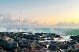 A fishing rod stands amid rocks as waves break on the shoreline at Poipu, Kauai, Hawaii