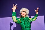 Confident senior woman in green against a violet background throwing up a confident pose.