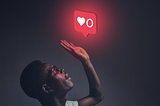 Young man in dimly lit room with hand reaching up to glowing ‘like’ icon