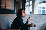 A photo of an Asian woman looking at her phone, cup in hand.