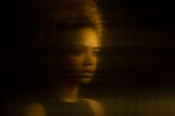 Distorted gold-tinted reflection of a young Black woman.