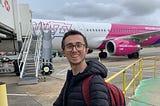 A man wearing a black jacket standing next to a Wizz Air A321 plane.