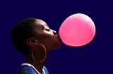 A photo of a young black woman wearing hoop earrings blowing a bubble with bubblegum.