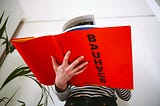 Photograph of someone in a striped artist’s jersey reading a big, bold red hardback book about the Bauhaus