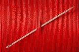 A needle stuck through a wall of red thread.