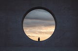 A person looking at a cloudy sky, sitting in a circular window that’s almost 10 times taller than them.
