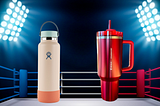 A peach Hydro Flask and a red Starbuck Stanley tumbler in a boxing ring