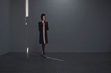 Woman walking in thin light stripe and looking up, in studio with concrete floor