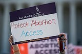 A woman holding up a sign that says “Protest Abortion Access.”