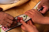 A photo of an elderly Ojibwe showing an embroidery to a young child.
