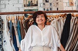 Woman smiling in front of a rack of clothes.