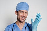 Male doctor grinning while putting on exam glove