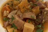 Shallow bowl of beef stew with large chunks of potato, garnished with chopped parsley.