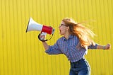 A person with long hair screaming into a megaphone.