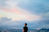 A man looks out at the sky and cityscape.