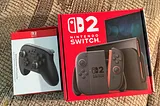 A Switch 2 Pro Controller Box (left) and a Switch 2 Box (right) sitting next to each other on my slightly ugly patterned couch.