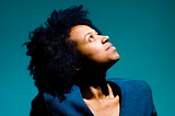 Black woman looking up against a teal background.