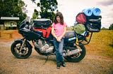 A photo of a young girl leaning against a motorbike that is loaded up with camping gear