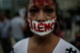 A woman with writing on her face that reads ‘no to silence’ looks at the camera during a demonstration in Mexico.