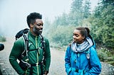 A smiling father and daughter stand and talk next to each other while preparing for early morning hike.