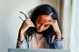 Shot of a young woman suffering from a headache while using a laptop at home.