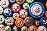 A stack of all different sizes and types of batteries, displayed with their cathodes facing forward