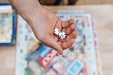 A hand holding two dice above a monopoly board game