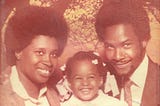 This is a studio photograph of a young girl between her parents with a tree in the background. Everyone is smiling. It is an old photo with a sepia tone that was taken in the early 1980's.