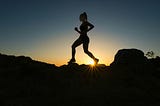 silhouette of a runner on a rocky ledge against a glowing sky