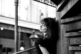 A black and white potrait of a woman standing on a balcony.