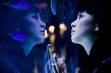 A woman at an aquarium looking at fishes in a tank. Cast in bluish light.