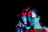 Two people standing close together in the dark with colorful, abstract shapes projected onto them.