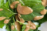 A photo of bright green spinach leaves coated in a creamy light brown balsamic dressing