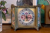 an old gilt clock, with a silk face embroidered with flowers, sat on a bookshelf.