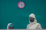 A photo of two healthcare workers wearing masks standing at a counter against a teal background.