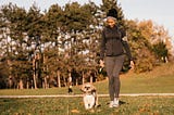 A photo of a black woman walking her dog at a park.