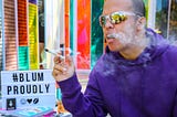 A person with a purple hoodie and sports sunglasses smoking a joint outside the Blüm storefront. #BlumProudly