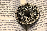 a coin with a Jewish dreidel sitting on a hebrew text