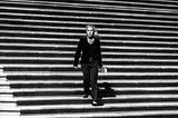 Marjorie Taylor Greene in a pantsuit walking down stone steps toward the camera. Black-and-white.