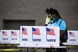 A photo of a black woman wearing a face mask voting at a poll booth in Kentucky.