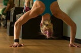 A woman is on her hands in a half handstand, with her feet up on a block behind her. She is in the middle of a pushup.