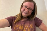 The author has long brown hair, glasses, a beard, a mustache, and is wearing a t-shirt that says “Love Y’all”. He has a mischievous smile that shows more in his tired eyes.