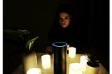 The author sits in the dark behind the Amazon Echo, which is surrounded by lit candles in a seance-style set up.