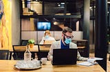 Businesspeople wearing masks in the office and sitting at further distances.