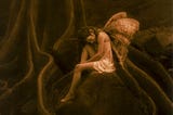 A sepia-toned image of a fairy sitting on a rock surrounded by tree roots