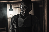 Mysterious figure in rustic setting with hanging light fixture — historical ambiance and storytelling vibe.