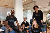 Image of five Indeed inclusion group members smiling and wearing shirts labeled “Women at Indeed” in a relaxed office setting